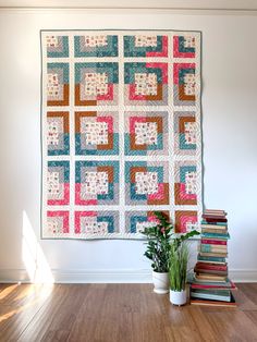 a quilted wall hanging on the wall next to a potted plant and books