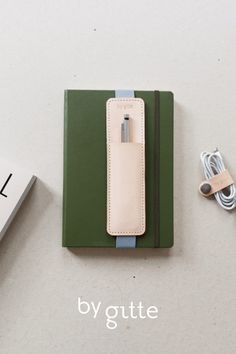 a green notebook with a white leather cover next to an earbud and charger