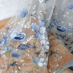 two sheer curtains with blue and white flowers are on a wooden table next to each other