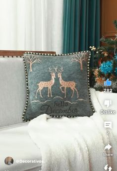 a christmas pillow sitting on top of a white couch next to a christmas tree and blue curtains