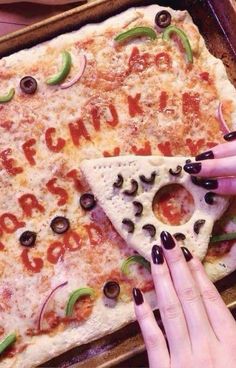 two hands reaching for a slice of pizza with letters and olives on it in a pan