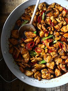 a white bowl filled with chicken and vegetables on top of a wooden table next to utensils