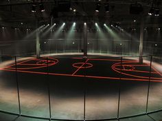 an empty basketball court with lights on the floor and in the middle is a cage