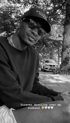 a man sitting on top of a bench next to a tree wearing sunglasses and a hat