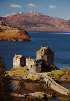 an old castle sitting on top of a hill next to a lake with mountains in the background