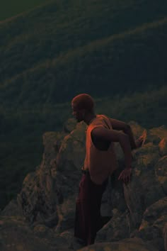 a man standing on top of a large rock next to a lush green hillside in the evening