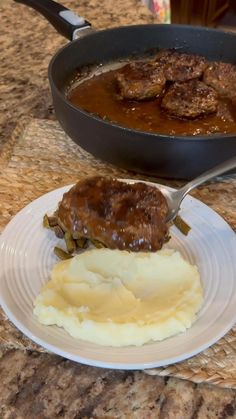 a plate with mashed potatoes, meat and gravy on it next to a skillet