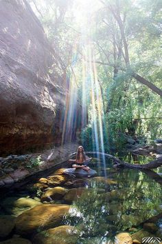 a person sitting on rocks in the middle of a stream with sunlight streaming through them