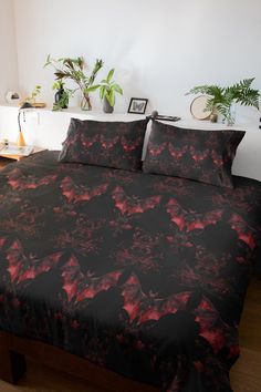 a bed covered in black and red sheets with plants on the headboard behind it