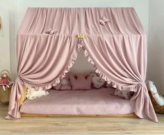 a pink canopy bed with curtains and stuffed animals