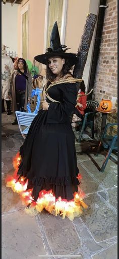 a woman dressed as a witch holding a broom and wearing a black dress with orange flames on the floor