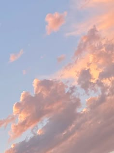 the plane is flying high in the sky with clouds behind it and pinkish colors