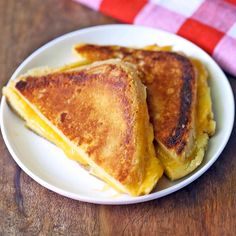 two pieces of grilled cheese on a white plate next to a red and white checkered napkin