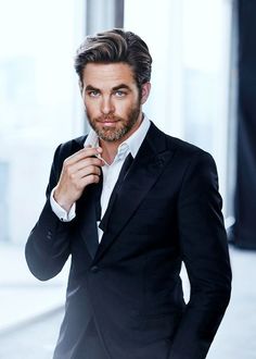 a man in a black suit and white shirt is posing for the camera with his hand on his tie