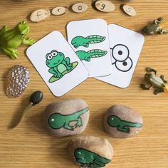 three cards with pictures of frogs and lizards on them, sitting next to rocks that spell out the word frog