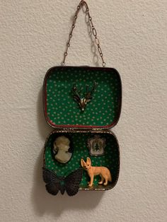 an open tin box with two little figurines in it on a chain hanging from the wall