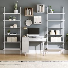 a computer desk sitting in front of a white book shelf filled with books and plants