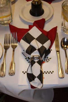 a white table topped with silverware next to a red and black checkered napkin