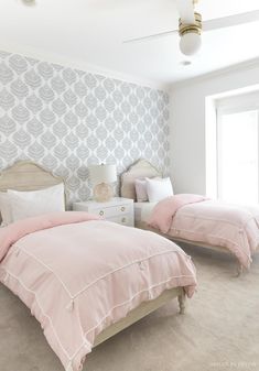 two beds in a bedroom with pink comforters and pillows on them, against a wallpapered background