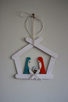 two colorful birds are hanging from a white frame with string and twine on the wall