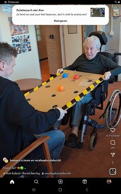 an old man in a wheelchair playing a board game with another person sitting at a table