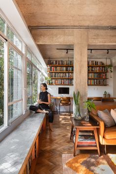 a woman sitting on a couch in a living room next to a book shelf filled with books