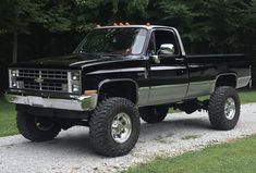 a black pickup truck parked on top of a gravel road next to some green trees