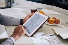 a man sitting at a table with an ipad in front of him and writing on the screen