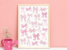 a pink watering can next to a framed print with bows on it and flowers in the vase