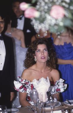 a woman sitting at a table in front of a group of people wearing tuxedos