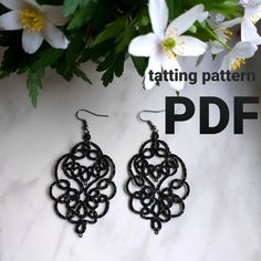 a pair of black earrings sitting on top of a marble table next to white flowers