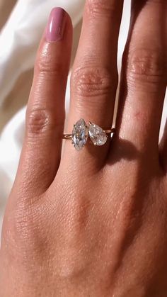 a woman's hand with a diamond ring on top of her left hand and a pink manicured nail