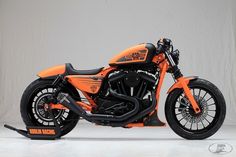 an orange and black motorcycle is parked in a white room with gray walls behind it