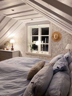 a bed with pillows and blankets in a bedroom under a slanted ceiling next to a window