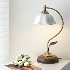 a desk lamp sitting on top of a white table next to a bouquet of flowers