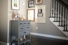 a room with stairs and pictures on the wall next to a dresser in front of a stair case