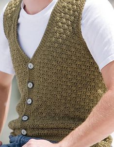 a man wearing a green knitted vest and white t - shirt is holding his hands in his pockets