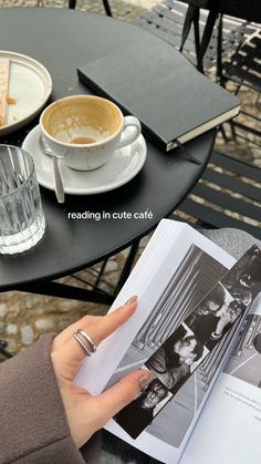 a person holding an open book in front of a cup of coffee on a table