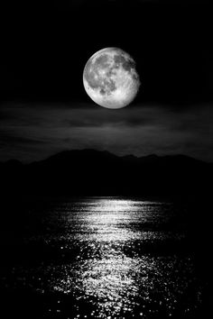 the full moon is reflected in the water on a dark night with mountains in the background