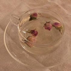 some pink flowers are floating in a glass bowl on a tableclothed surface,