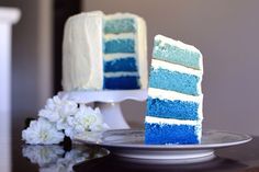 a blue ombre cake sitting on top of a plate next to a vase with flowers