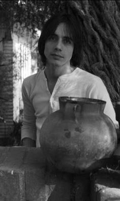 black and white photograph of a woman leaning on a wall holding a large vase in front of her face