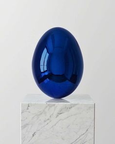 a blue glass ball sitting on top of a marble block in front of a white wall