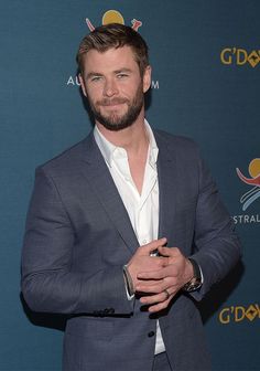 a man in a suit and white shirt posing for the camera with his hand on his chest