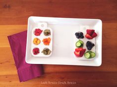 two trays filled with fruit and vegetables on top of a wooden table next to a purple napkin