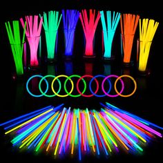 neon glow sticks are arranged next to cups with straws in them on a black background