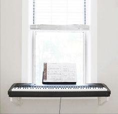 an electronic keyboard sitting on top of a window sill in front of a white wall