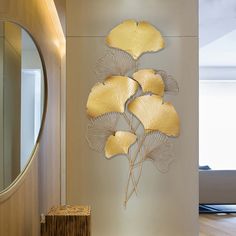 a metal wall sculpture with yellow leaves on it in a living room area next to a mirror