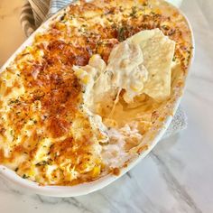 a white dish filled with food on top of a marble counter next to a fork