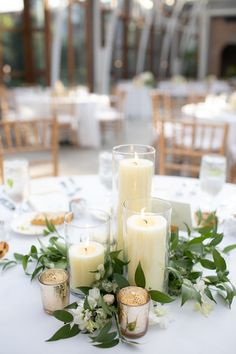 candles and greenery are arranged on the table for a centerpiece at this wedding reception